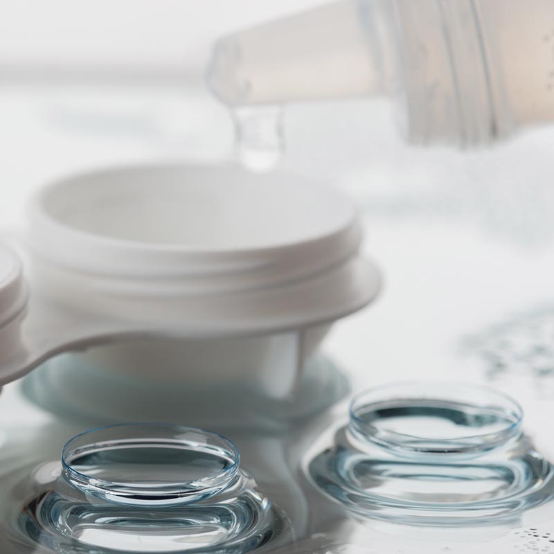 Closeup of soft contact lens with contact lens case and solutions